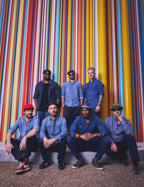 le groupe de 7 hommes se tients devant un ensemble de tuyaux aux couleurs différentes